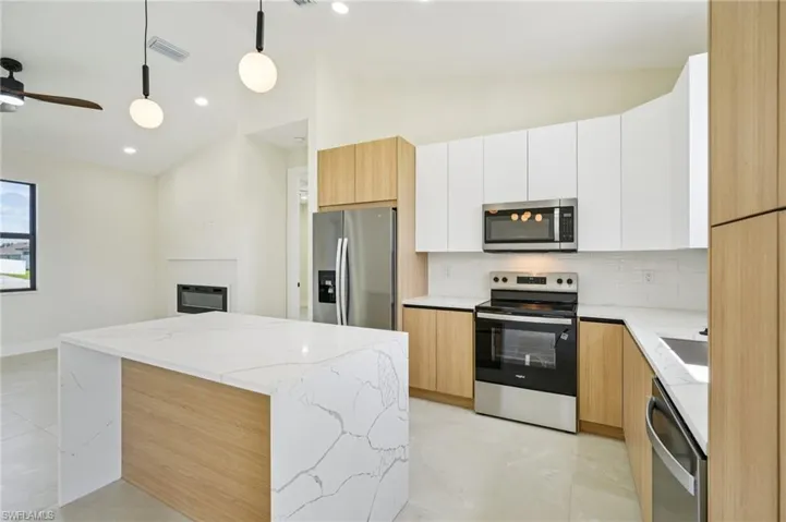 Kitchen featuring modern cabinets, light stone counters, appliances with stainless steel finishes, white cabinets, and pendant lighting