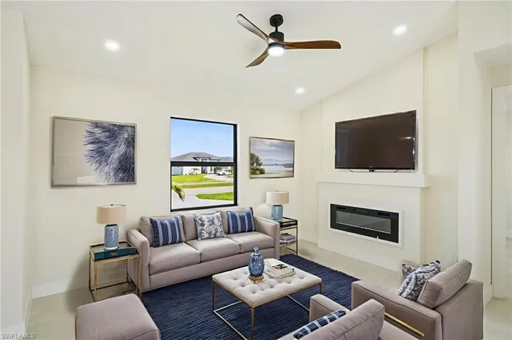 Living room with recessed lighting, lofted ceiling, a ceiling fan, a glass covered fireplace, and light tile patterned flooring