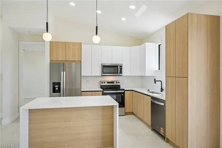 Kitchen with stainless steel appliances, modern cabinets, pendant lighting, light stone counters, and lofted ceiling