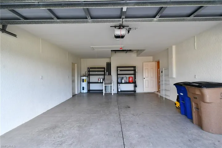 Garage with a textured wall, water heater, and a garage door opener