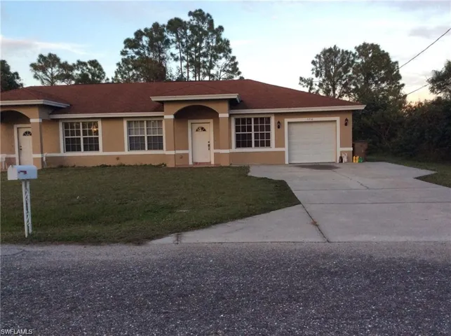 Duplex property featuring a neutral stucco exterior, a red-tiled roof, multiple white-framed windows, and an attached garage with a concrete driveway
