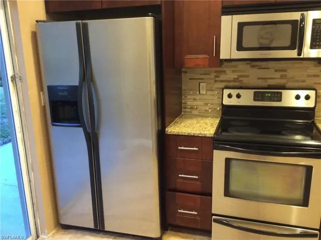 Stainless steel side-by-side refrigerator, stainless steel electric range, stainless steel microwave, stone countertop, and mosaic tile backsplash