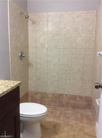 Integrated shower area with tiled walls and flooring, featuring a wall-mounted shower head and control