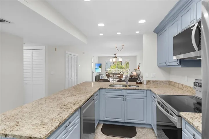 Kitchen featuring appliances with stainless steel finishes, a peninsula, recessed lighting, light stone counters, and hanging light fixtures