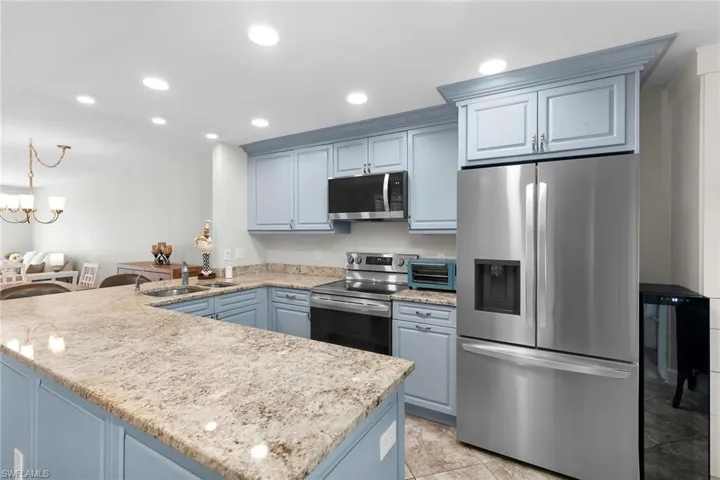 Kitchen with appliances with stainless steel finishes, a peninsula, recessed lighting, light stone countertops, and blue cabinets