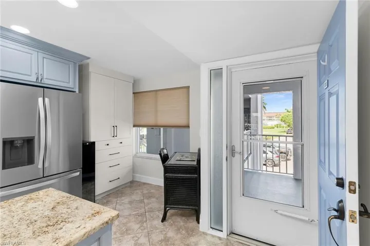 Kitchen with stainless steel fridge, light tile patterned floors, and white cabinetry