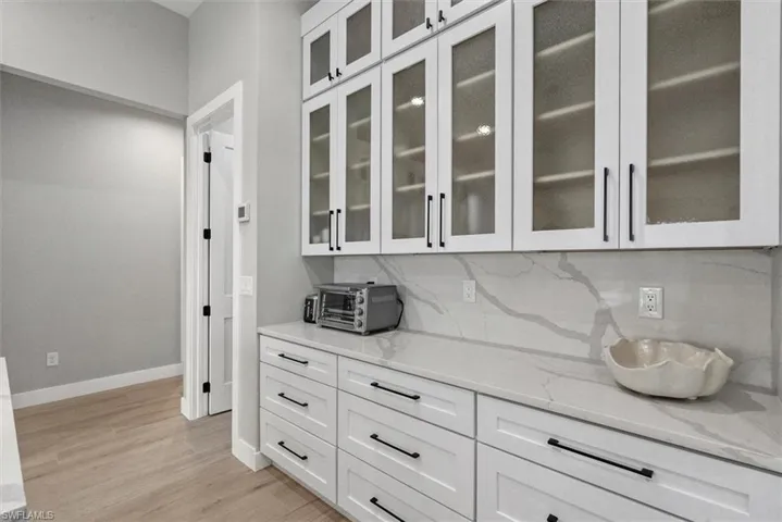 Bar with white cabinetry, light stone countertops, glass insert cabinets, and light wood-style floors