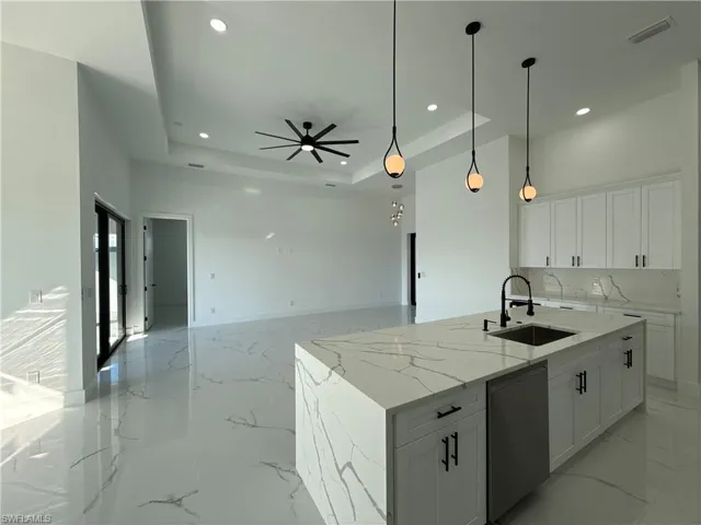 Kitchen with white cabinetry, light stone countertops, stainless steel dishwasher, hanging light fixtures, and a center island with sink