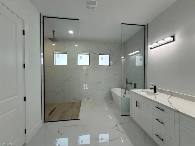 Bathroom featuring a marble finish shower, vanity, a soaking tub, recessed lighting, and stone wall