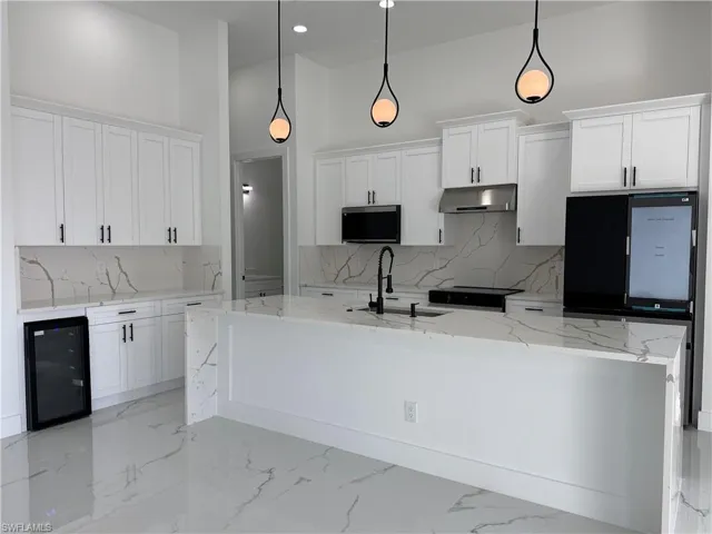 Kitchen with light stone countertops, a high ceiling, beverage cooler, white cabinets, and refrigerator