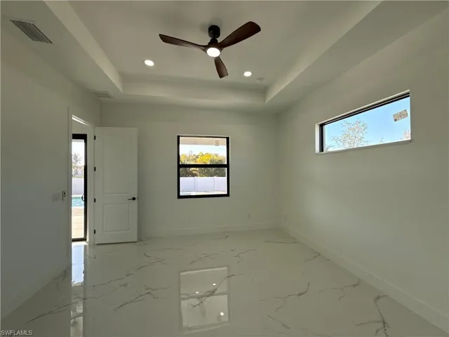 Empty room with a ceiling fan, light marble finish flooring, recessed lighting, and a raised ceiling