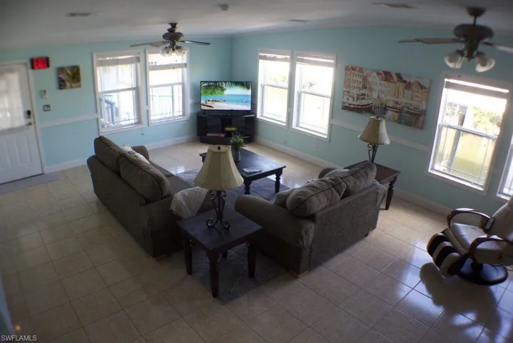 Living area featuring a ceiling fan, light tile patterned flooring, and lofted ceiling