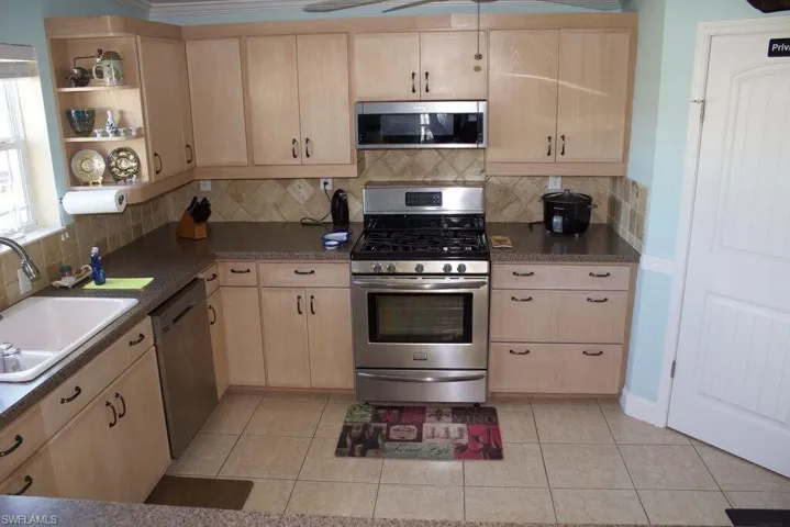 Kitchen featuring appliances with stainless steel finishes, light brown cabinetry, decorative backsplash, light tile patterned floors, and open shelves