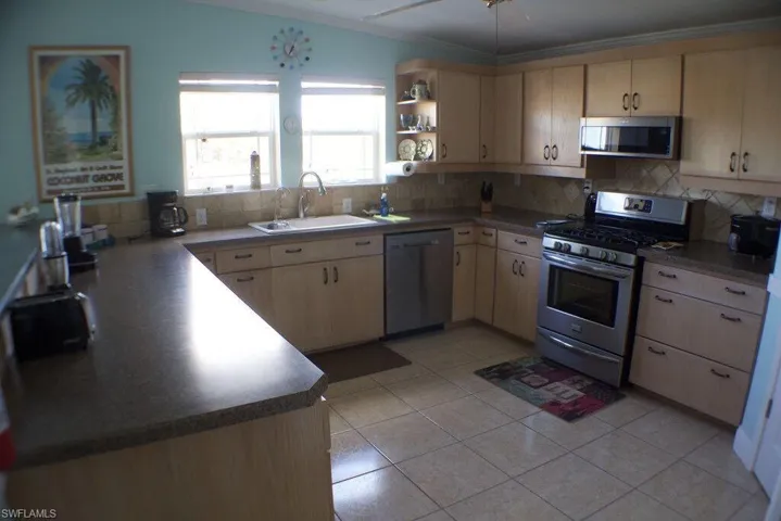 Kitchen featuring appliances with stainless steel finishes, backsplash, ornamental molding, light brown cabinets, and open shelves