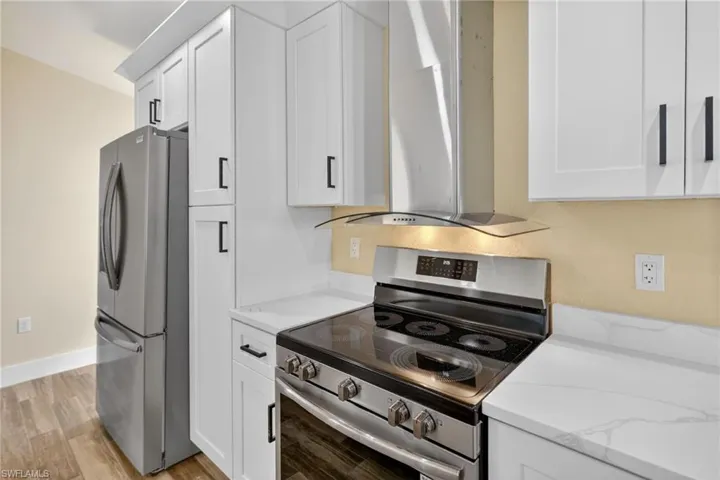 Kitchen with stainless steel appliances, white cabinets, island range hood, and light stone counters