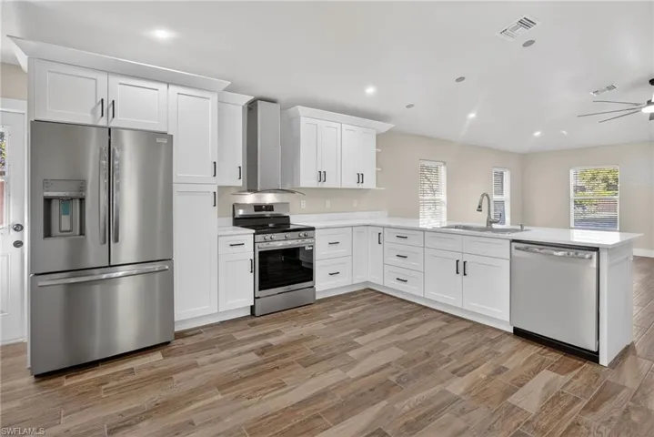 Kitchen with appliances with stainless steel finishes, white cabinetry, recessed lighting, a peninsula, and range hood