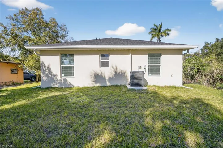 Rear view of property featuring a lawn and stucco siding