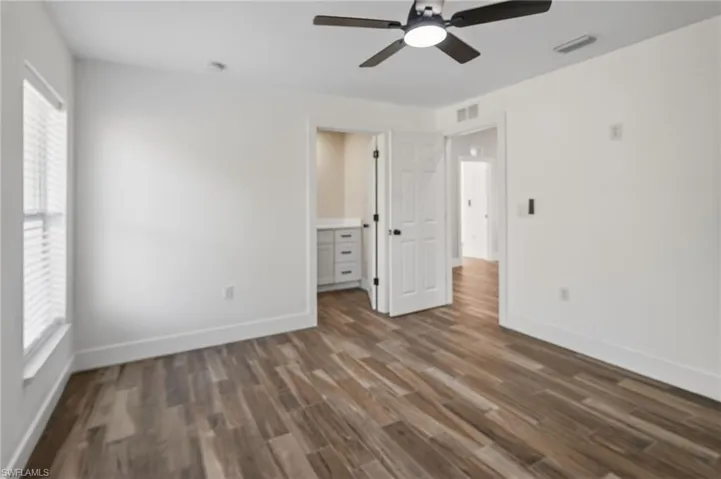 Unfurnished bedroom featuring dark wood-style flooring, a ceiling fan, and ensuite bathroom