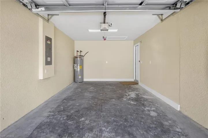 Garage with a textured wall, water heater, electric panel, and a garage door opener