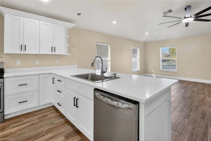 Kitchen with wood tiled floors, stainless steel dishwasher, white cabinetry, open shelves, and a peninsula