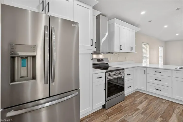 Kitchen featuring stainless steel appliances, white cabinetry, recessed lighting, wall chimney exhaust hood, and wood tiled floors