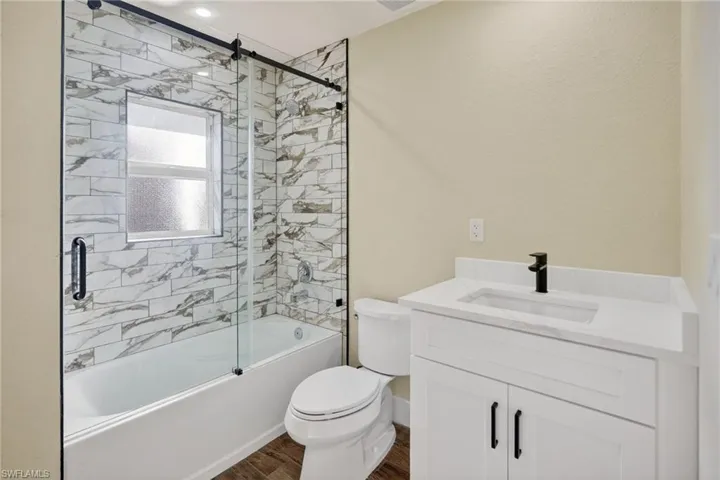 Full bathroom with vanity, dark wood-type flooring, and bath / shower combo with glass door