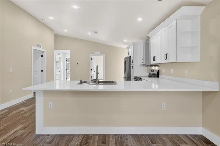 Kitchen with a peninsula, open shelves, white cabinetry, stainless steel appliances, and light stone countertops