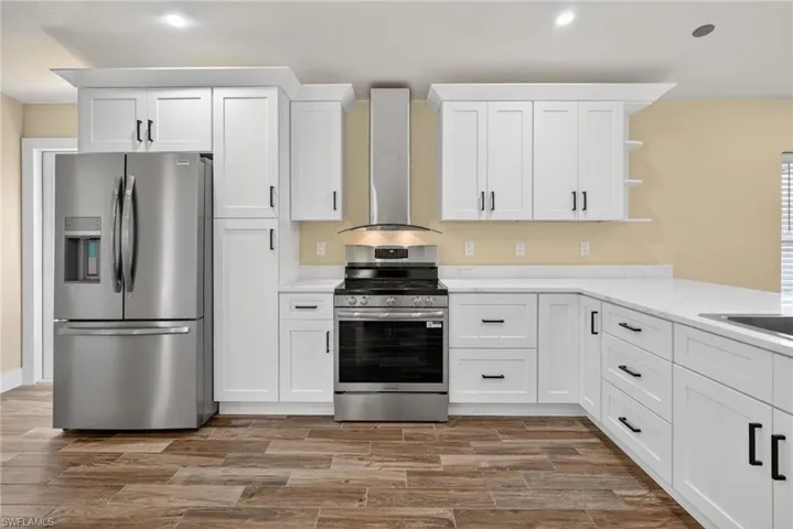 Kitchen with appliances with stainless steel finishes, white cabinetry, wall chimney exhaust hood, open shelves, and recessed lighting