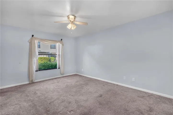 Carpeted spare room featuring ceiling fan and baseboards
