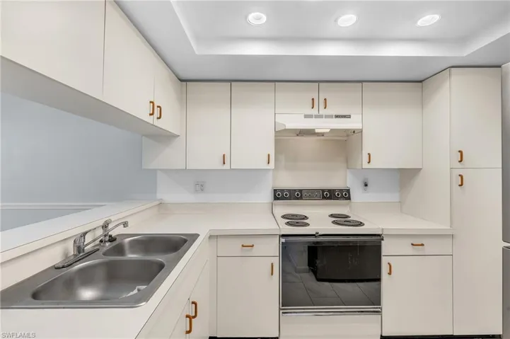 Kitchen with range with electric stovetop, light countertops, under cabinet range hood, a tray ceiling, and recessed lighting
