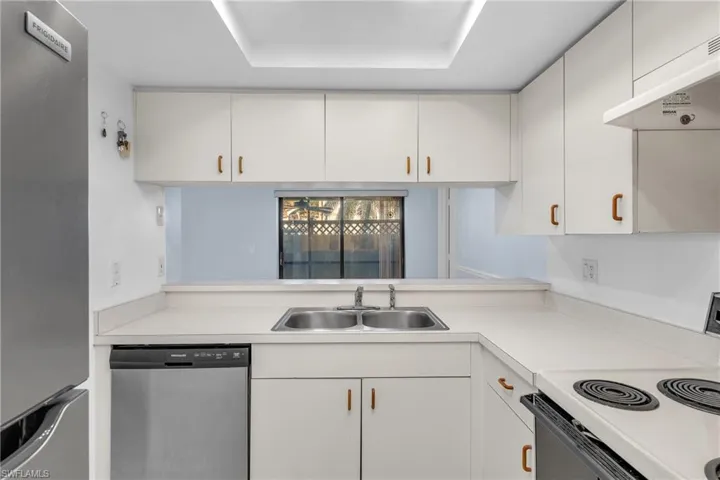 Kitchen with stainless steel appliances, light countertops, under cabinet range hood, white cabinetry, and a raised ceiling