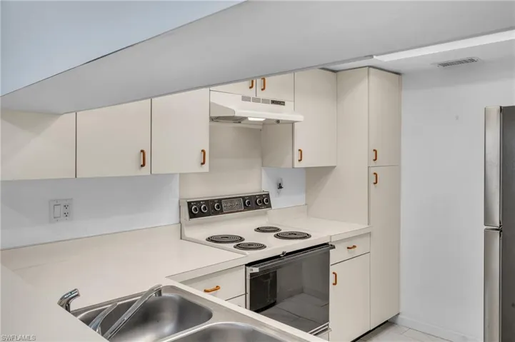 Kitchen featuring range with electric stovetop, light countertops, freestanding refrigerator, under cabinet range hood, and white cabinetry