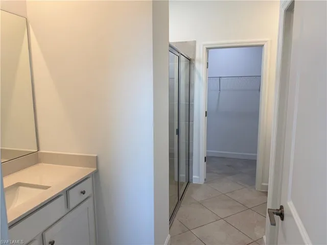Bathroom featuring a vanity with a light-toned countertop, a frameless mirror, a glass-enclosed shower, tile flooring, and a walk-in closet with built-in shelving
