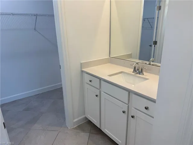Vanity featuring white shaker-style cabinetry, a light-toned solid surface countertop, an integrated rectangular sink, chrome-finish faucet, and a large wall-mounted mirror, finished with oversized tile flooring