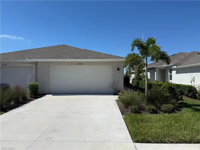 Single-story exterior featuring a stucco facade, concrete driveway, attached two-car garage, and established landscaping with palm trees