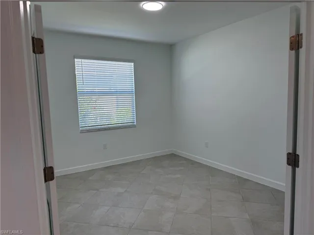 Interior room featuring large-format tile flooring, double door entry, and a window with integrated blinds