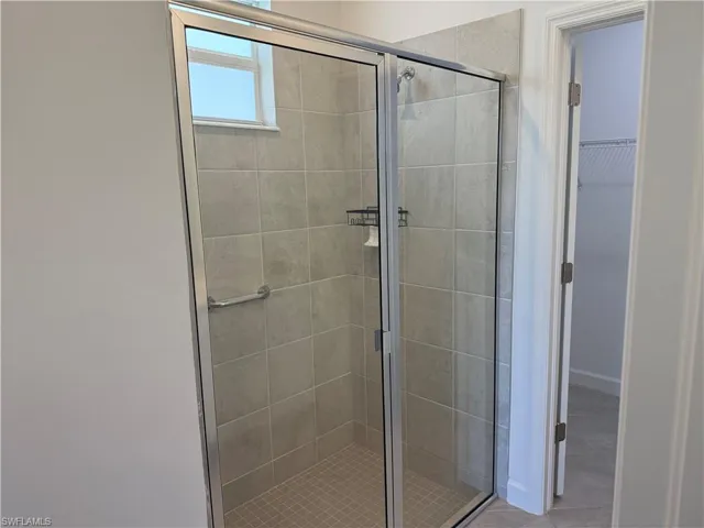 Walk-in shower featuring a framed glass enclosure, neutral tile surround, grid-patterned floor tile, and integrated shelving