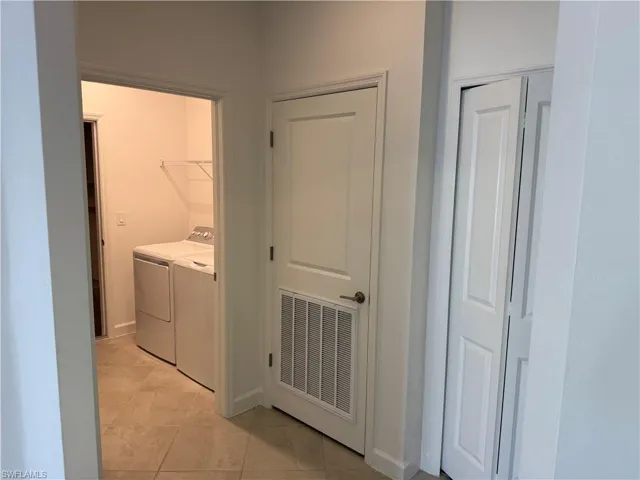 Laundry area featuring tile flooring, neutral wall tones, bi-fold closet doors, and an interior door with a built-in ventilation grate