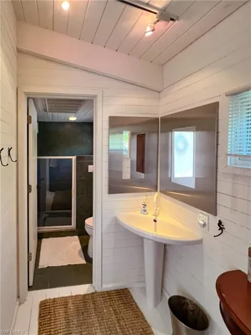 Bathroom with wooden walls, toilet, tile patterned flooring, and vaulted ceiling
