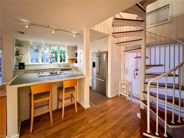 Kitchen with wood-type flooring, stainless steel appliances, white cabinets, rail lighting, and stainless steel counters