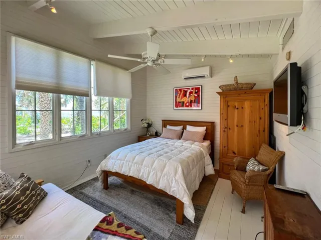 Bedroom with vaulted ceiling with beams, an AC wall unit, ceiling fan, and hardwood / wood-style flooring
