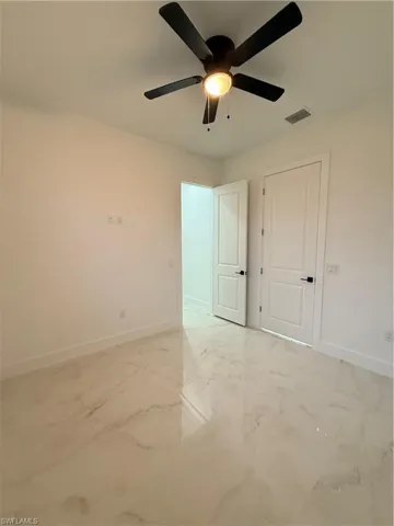 Empty room with a ceiling fan and light marble finish floors