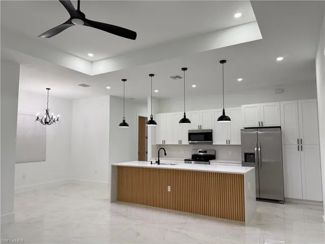 Kitchen with appliances with stainless steel finishes, light marble finish flooring, recessed lighting, light countertops, and a kitchen island with sink