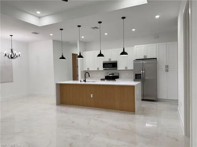Kitchen featuring appliances with stainless steel finishes, light marble finish flooring, light countertops, a center island with sink, and recessed lighting