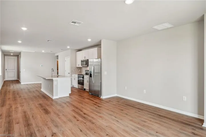 Kitchen with light hardwood / wood-style floors, white cabinets, decorative backsplash, a center island with sink, and appliances with stainless steel finishes