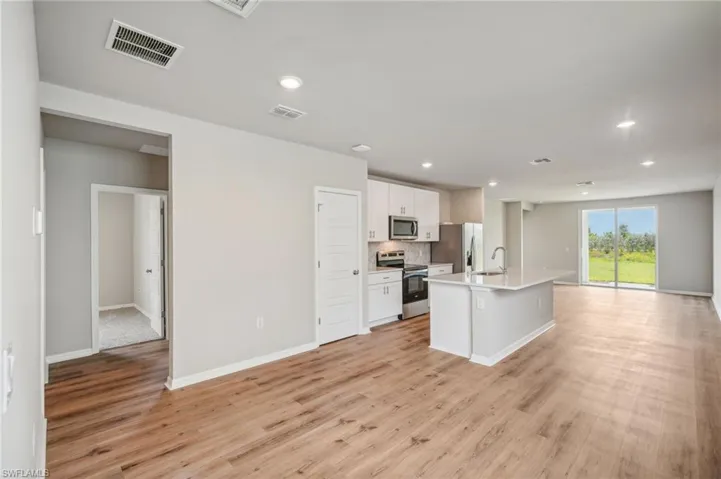 Kitchen featuring light hardwood / wood-style floors, sink, white cabinetry, a center island with sink, and appliances with stainless steel finishes