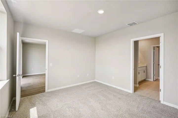 Unfurnished bedroom featuring light carpet and connected bathroom