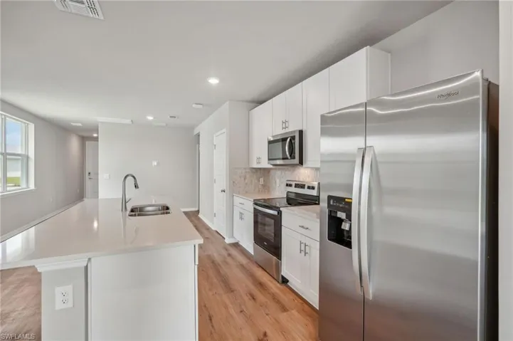 Kitchen featuring white cabinets, stainless steel appliances, light wood-type flooring, a kitchen island with sink, and sink