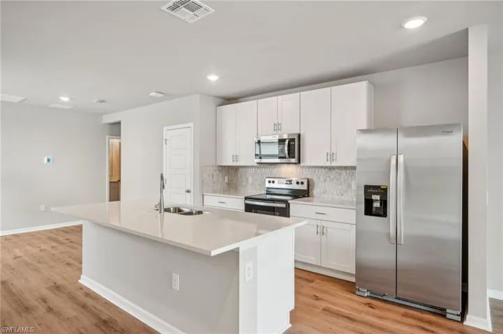 Kitchen with appliances with stainless steel finishes, white cabinetry, sink, and an island with sink