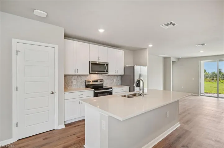 Kitchen with appliances with stainless steel finishes, white cabinetry, an island with sink, light wood-type flooring, and sink